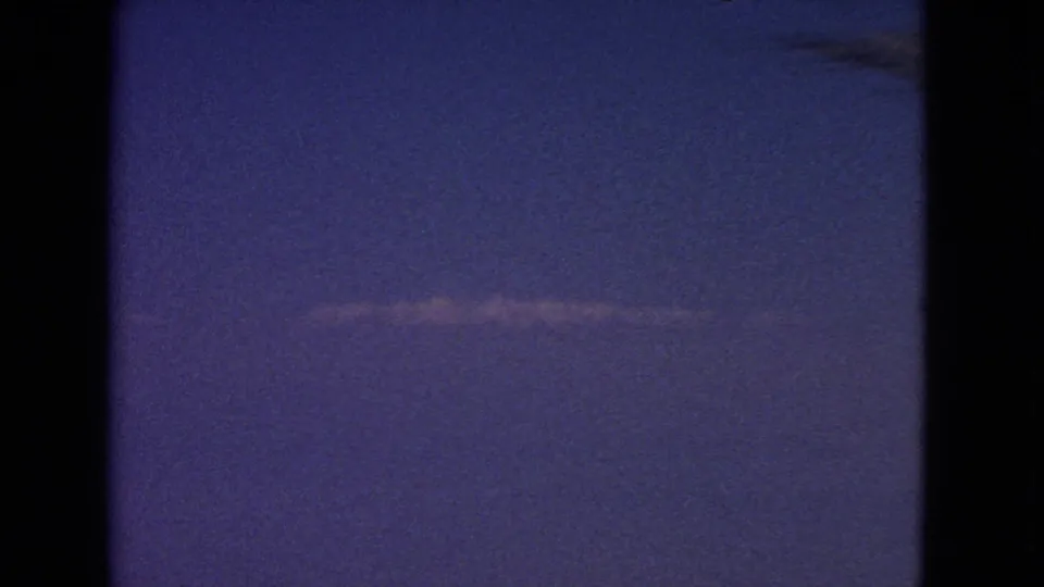 1963 8mm frame showing a thin contrail across a blue-purple sky, with dark window or film-edge borders.
