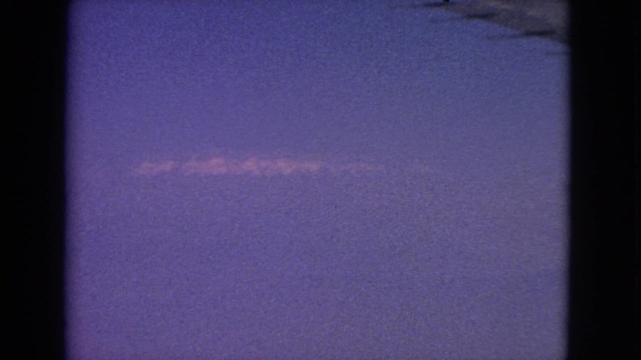 1963 8mm airplane-window view with a small wing section at upper right and a pale contrail across the sky.