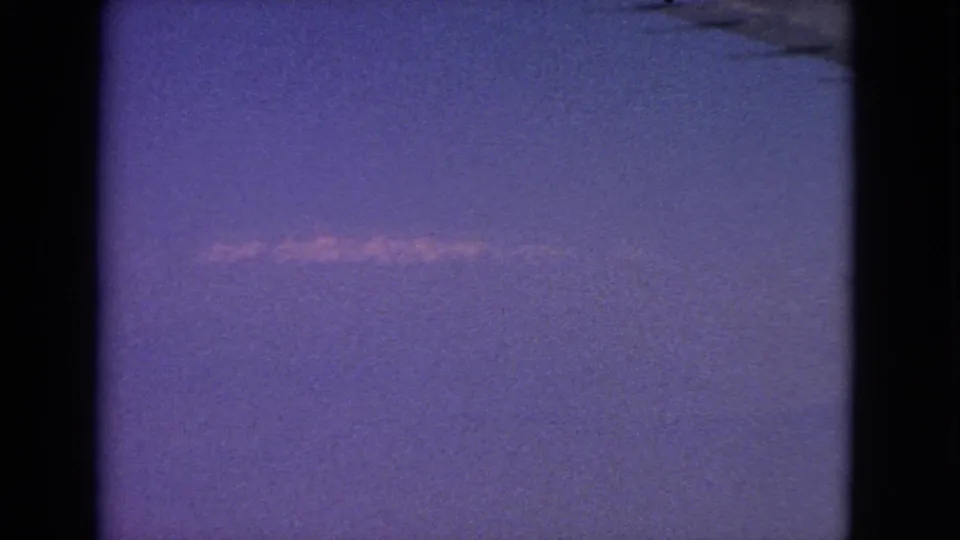 1963 8mm airplane-window view with a small wing section at upper right and a pale contrail across the sky.
