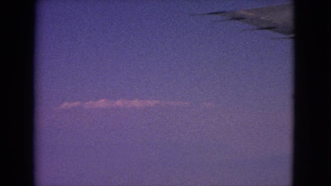 Purple dusk sky seen through an airplane window with a faint contrail and wing silhouette.