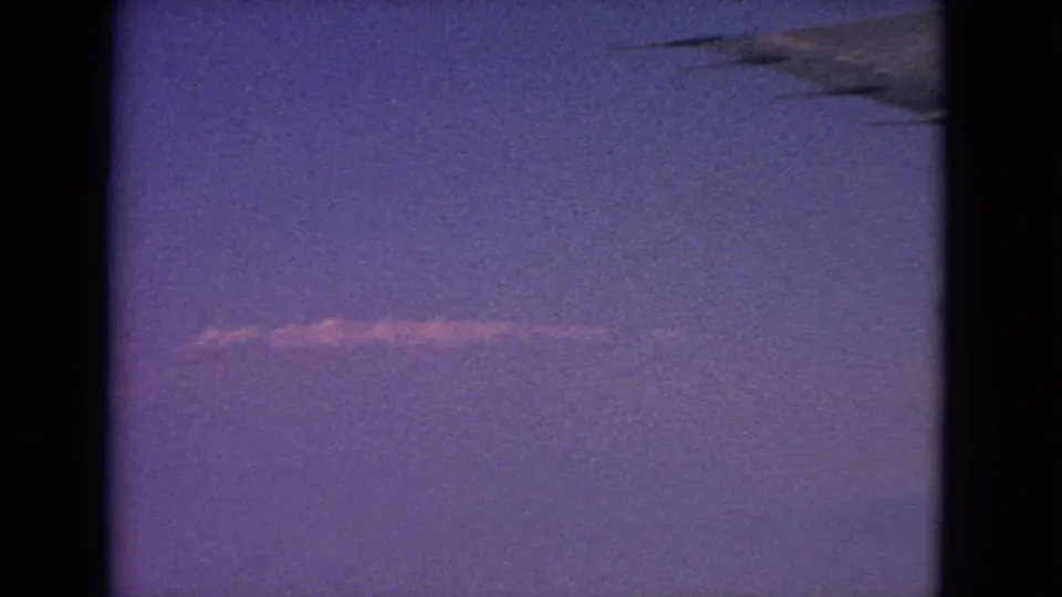 1963 8mm airplane-window view near Barrington, Illinois, showing purple twilight sky, a faint contrail, and a dark wing edge.