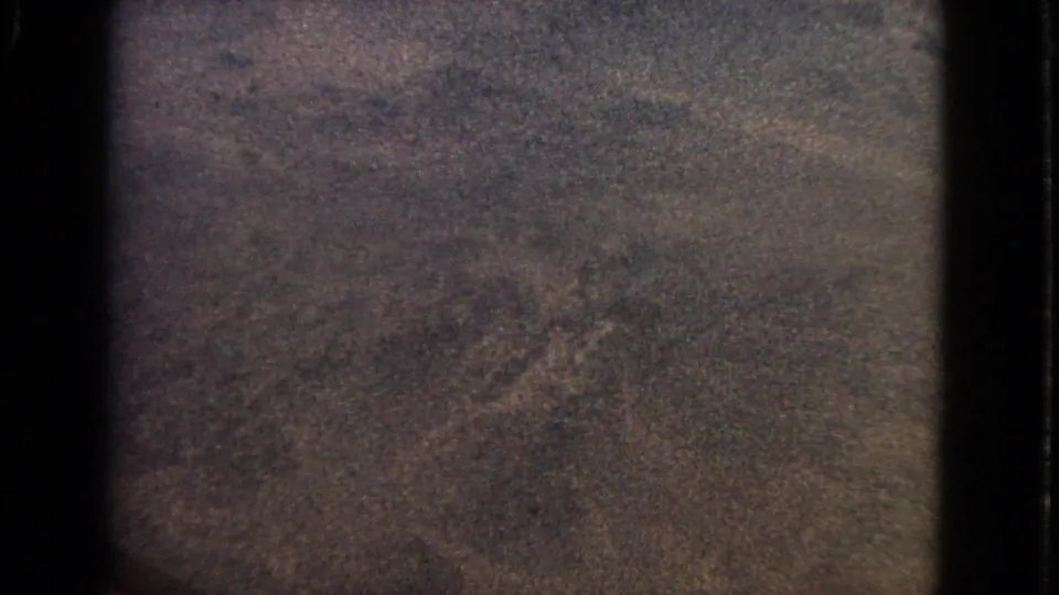 Grainy 8mm low-light airplane-window footage from 1963, showing dark borders and indistinct dusk texture below or beyond the window.