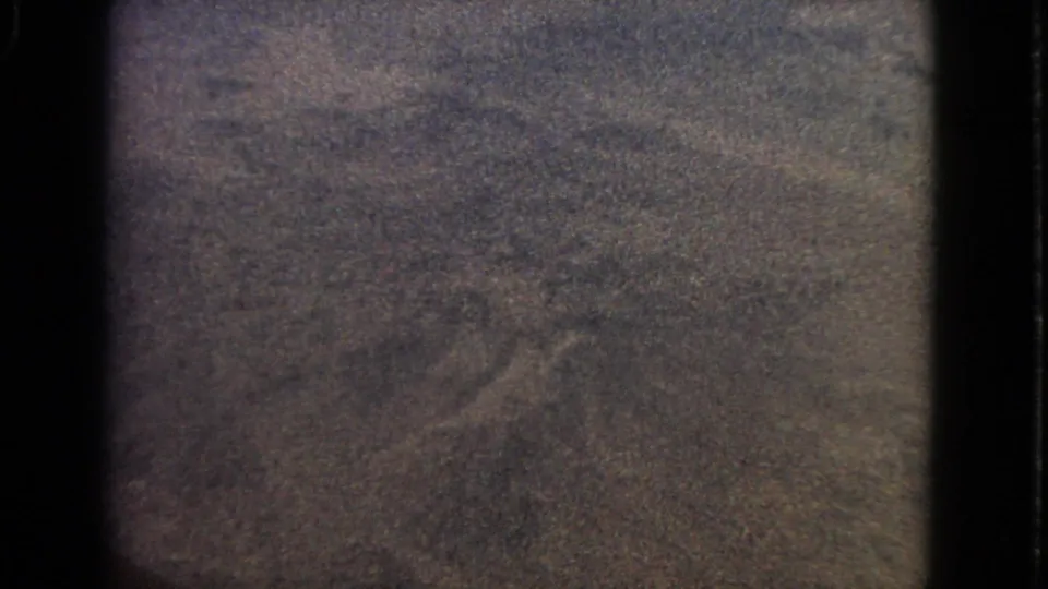 The 1963 8mm airplane-window view remains dim and grainy, with dark frame edges and indistinct twilight detail.