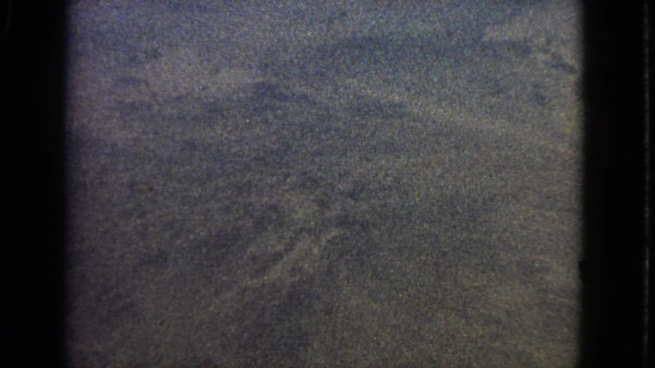 Grainy aerial view through a dark airplane-window frame.
