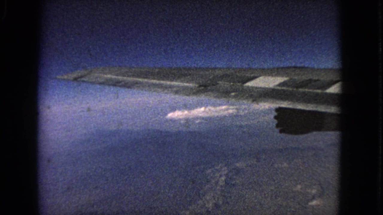 Airplane wing stretches across a blue sky with clouds and terrain far below.