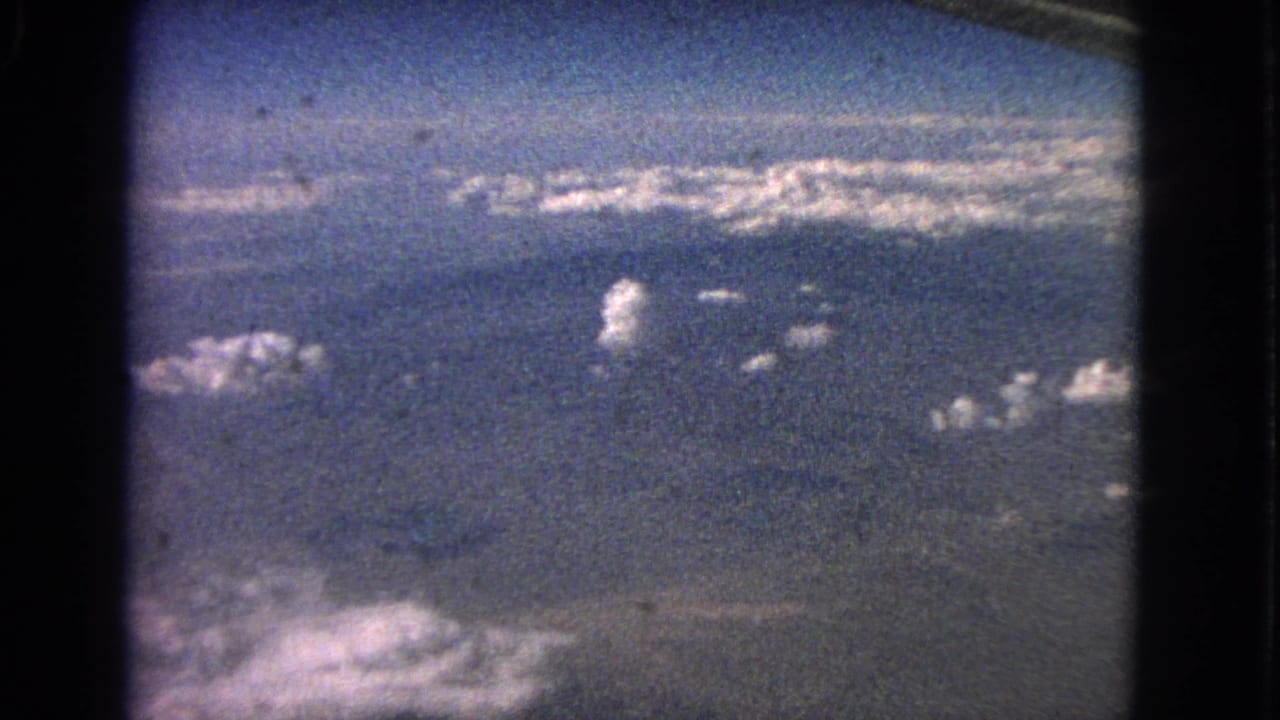 Steady 1963 aerial home-movie frame looking out over clouds, blue sky, and faint lower landscape or water.
