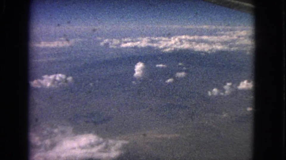 Steady 1963 aerial home-movie frame looking out over clouds, blue sky, and faint lower landscape or water.
