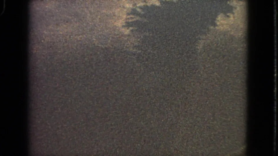 Grainy 8mm frame from the airplane-window sequence, with cloud forms and a darker lower area that appears to be terrain or water.