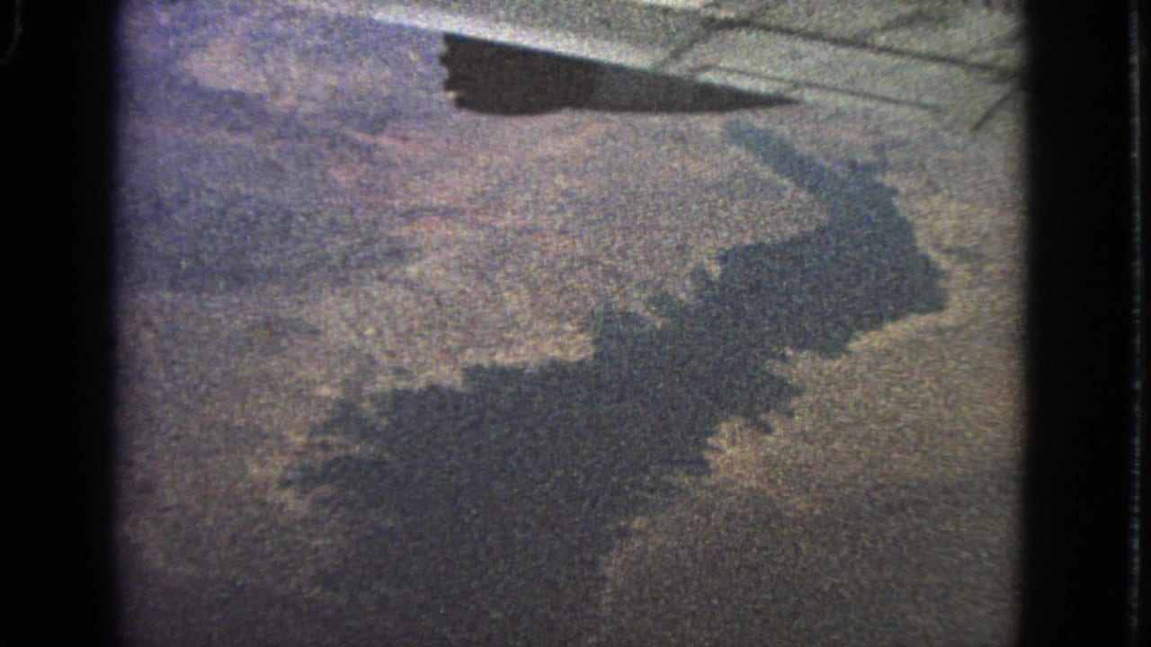 Airplane wing shadow crossing land and water seen from a window.