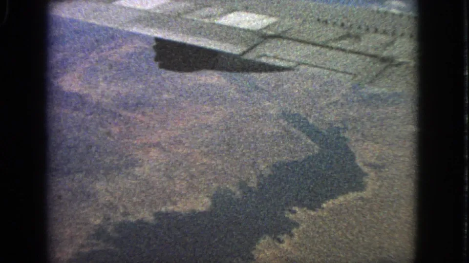 The final frame keeps the window-seat perspective, with a dark plane shadow sliding across land and water beneath the wing.