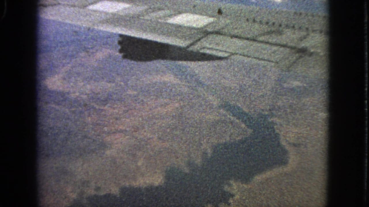 1963 8mm passenger-window view near Barrington, Illinois, showing an airplane wing and shadow over land.