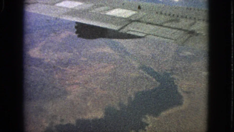 1963 8mm passenger-window view near Barrington, Illinois, showing an airplane wing and shadow over land.