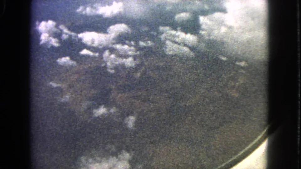 Passenger-window aerial view from 1963, showing clouds over indistinct land with visible 8mm film grain.
