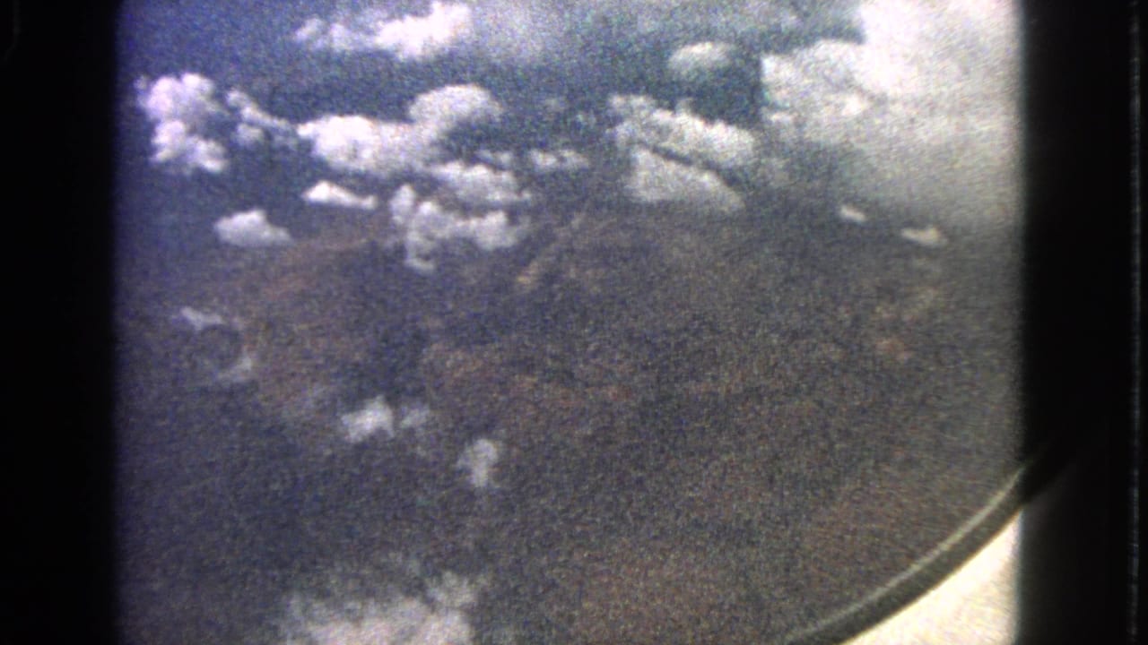 Cataloged 1963 8mm frame showing clouds and darker terrain below through an airplane window.