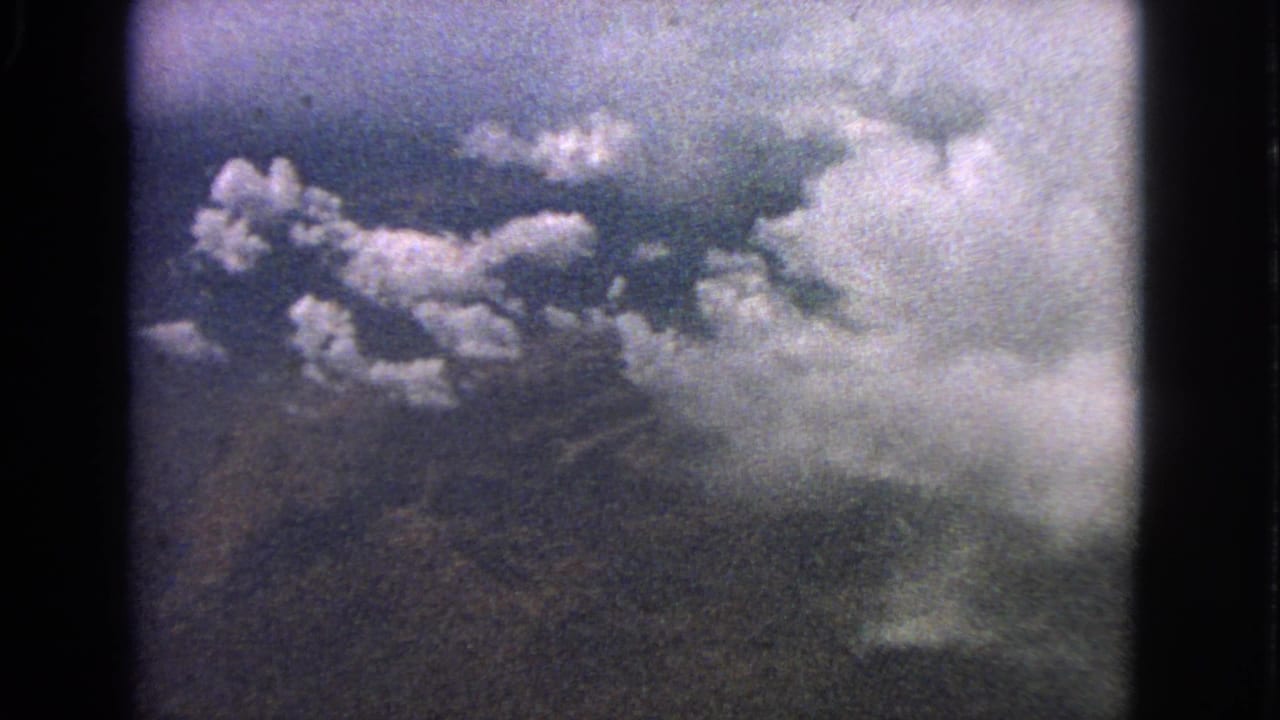 Clouds and dark ground seen through a plane window on grainy 8mm film.