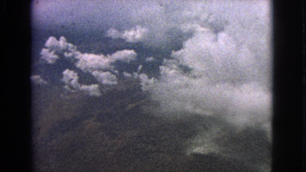 1963 8mm frame from an airplane window near Barrington, Illinois, with cumulus clouds over a muted landscape.