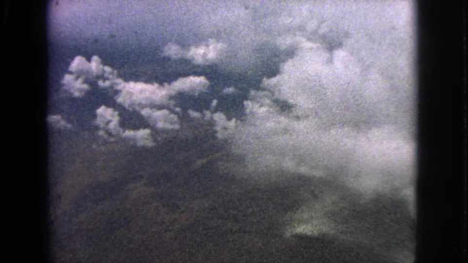 1963 8mm frame from an airplane window near Barrington, Illinois, with cumulus clouds over a muted landscape.