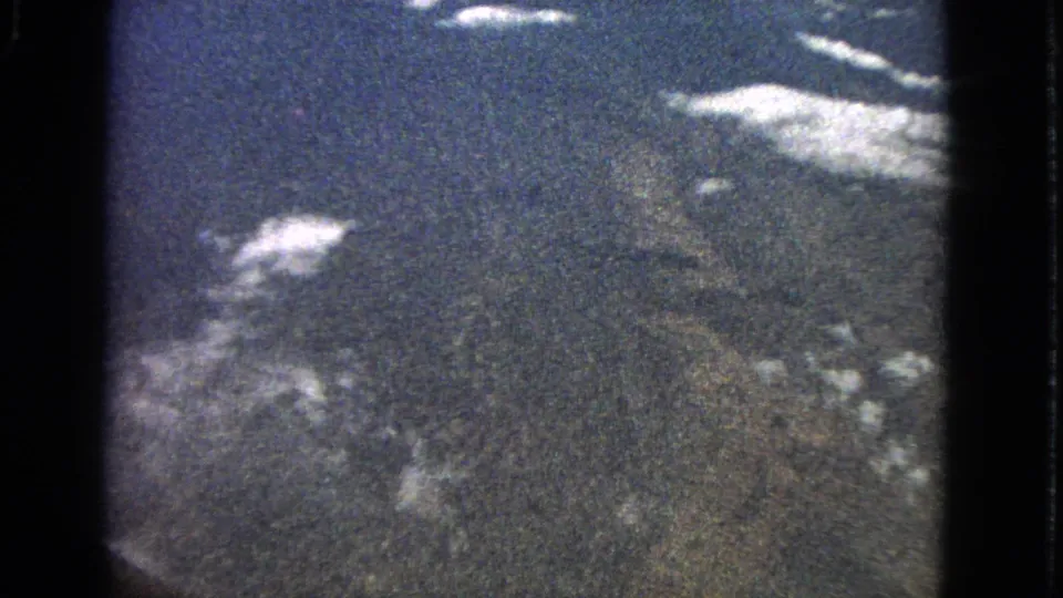 Grainy 1963 8mm airplane-window view near Barrington, Illinois, looking across bright clouds and distant ground.