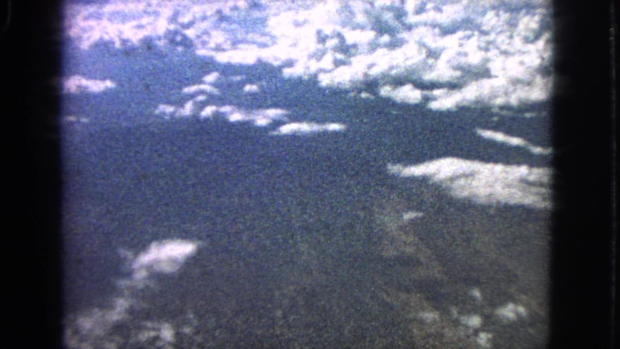 High-altitude view of scattered clouds and dark ground framed by black film or window edges.