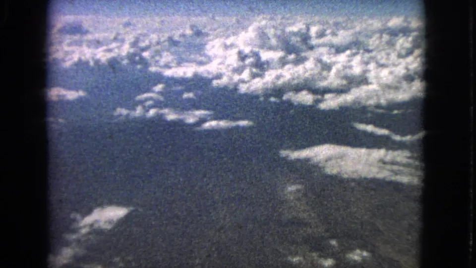 1963 8mm home-movie frame showing bright cloud cover and dark terrain below from an airplane perspective.