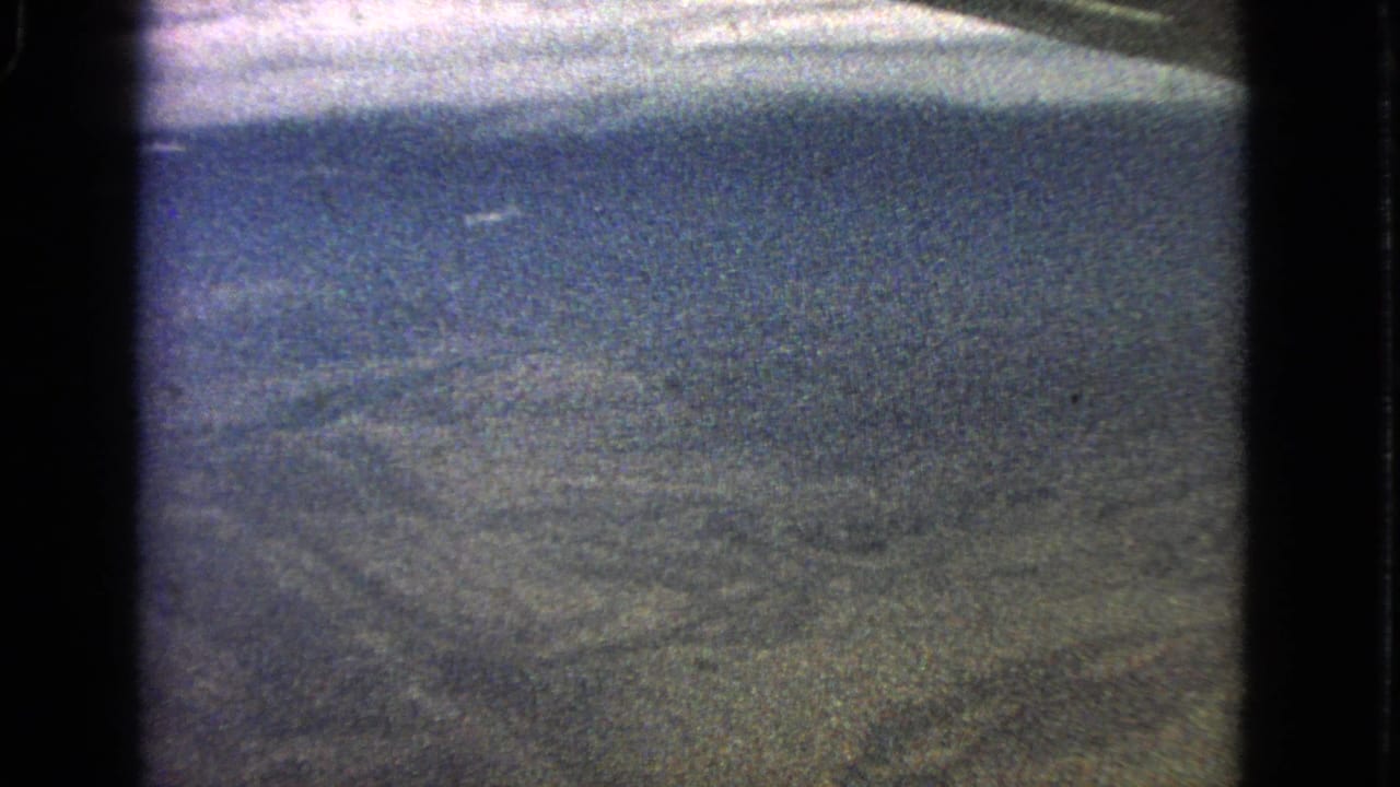 Grainy view from an airplane window over hazy arid terrain.