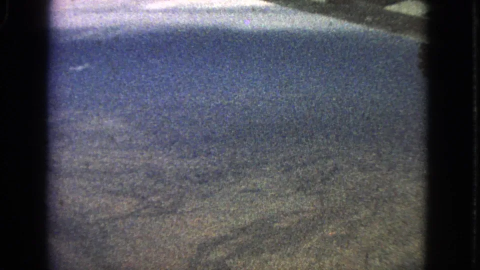 Vintage 8mm frame with a blurred aerial view of open terrain, partially bordered by the aircraft window frame.