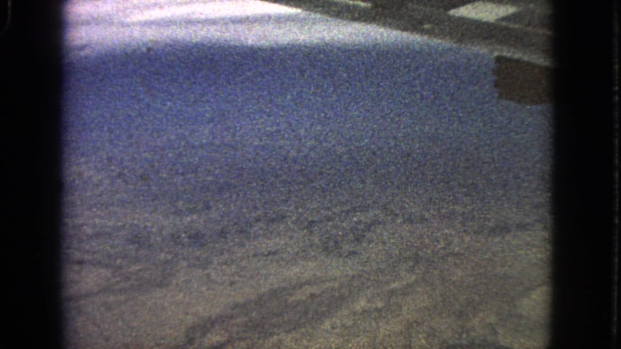 Grainy aerial view through dark aircraft-window edges with hazy terrain below.