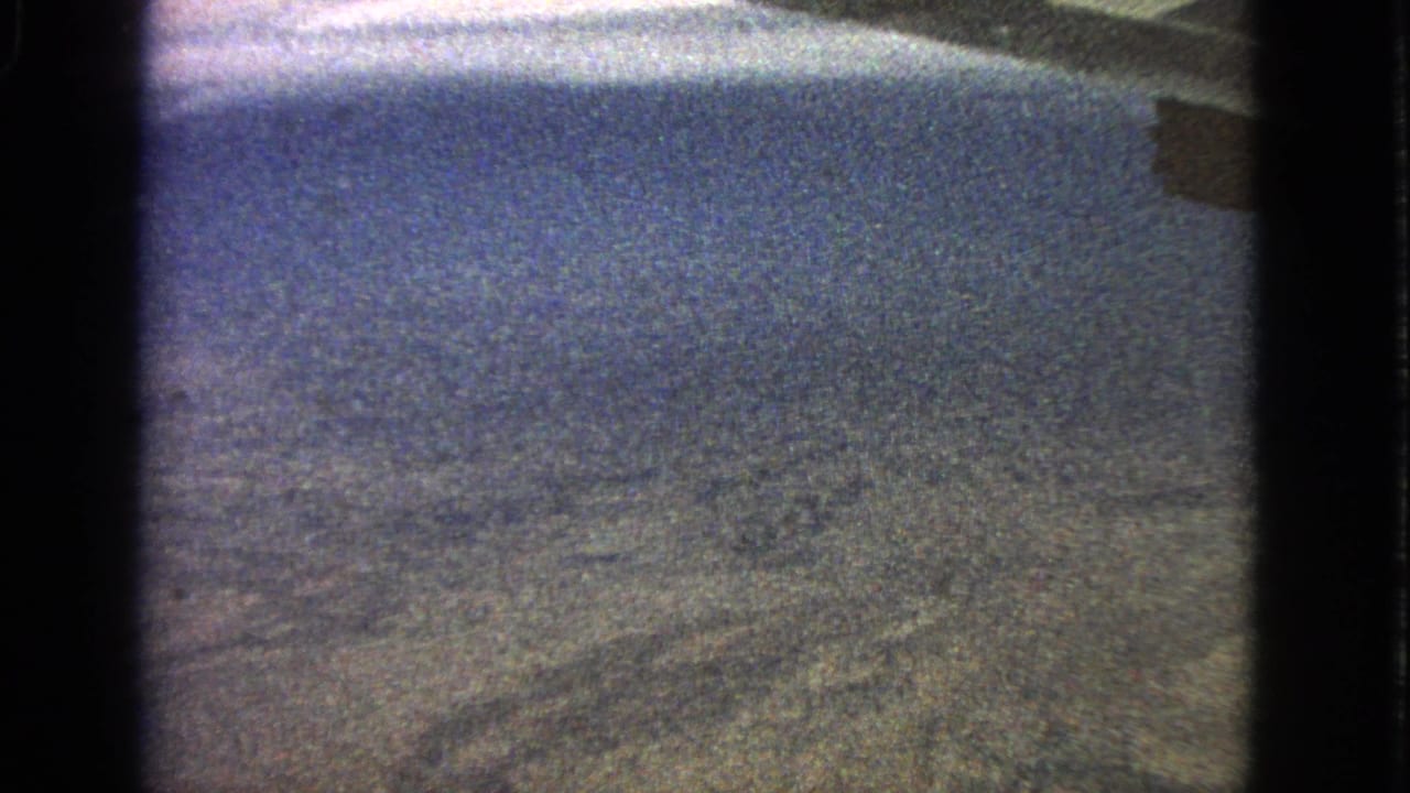 Soft aerial view of distant terrain and sky framed by dark vertical window edges.