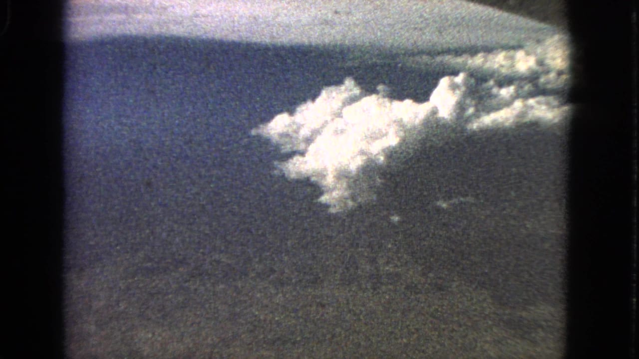 1963 8mm aerial view associated with Barrington, Illinois, showing bright clouds above dark land and a blue horizon.