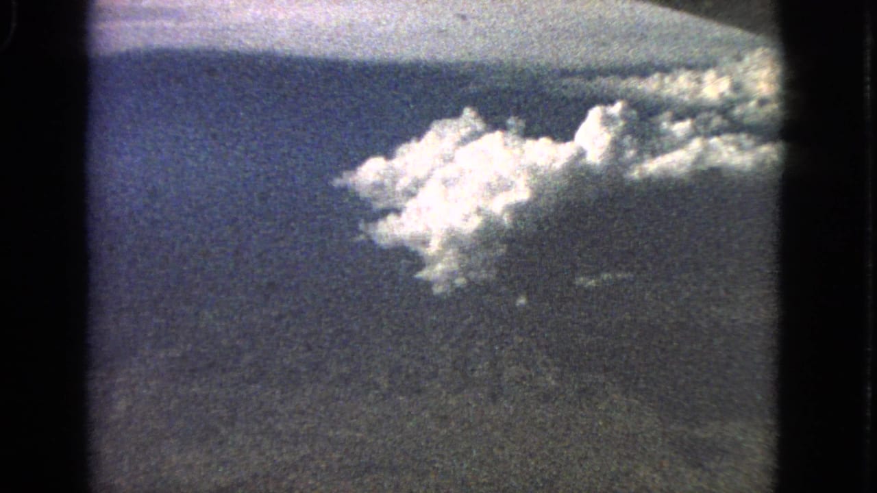 1963 8mm aerial frame tied to Barrington, Illinois, with white clouds drifting above dark terrain and a soft horizon.