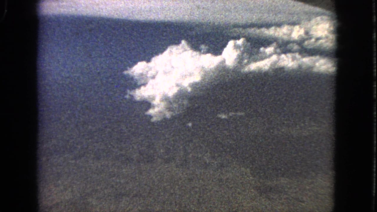 Bright clouds and dark sky band within a soft, grainy film frame.