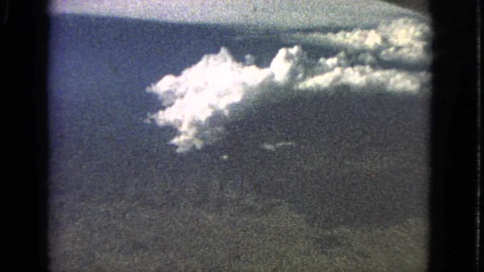 1963 8mm in-flight view showing a bright cumulus cloud, blue sky, and darker cloud texture beneath it.