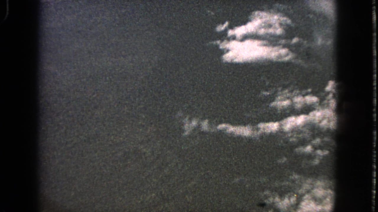 1963 8mm home-movie frame showing a dark aerial sky with bright cloud formations and soft film-frame edges.