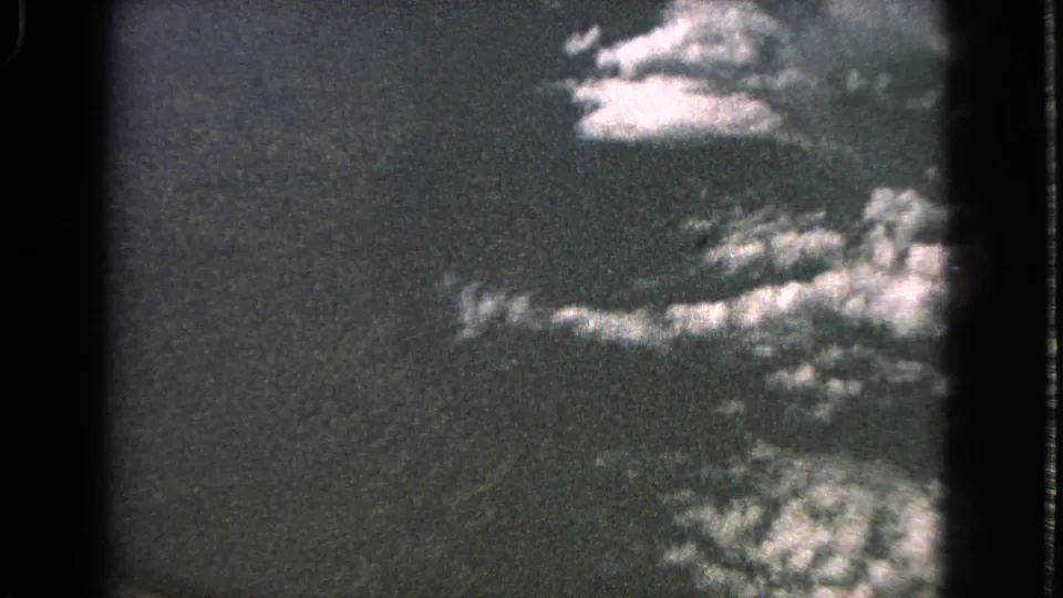 1963 8mm aerial view with scattered bright clouds, dark sky, and visible gate-edge shadowing.