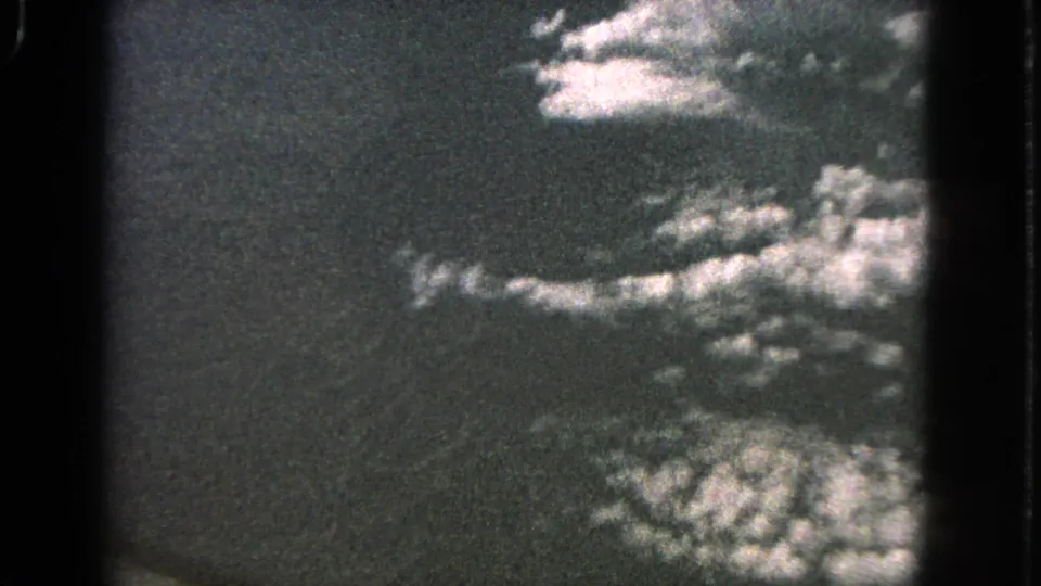 1963 8mm home-movie frame showing a soft aerial cloudscape with dark sky and possible faint ground texture below.