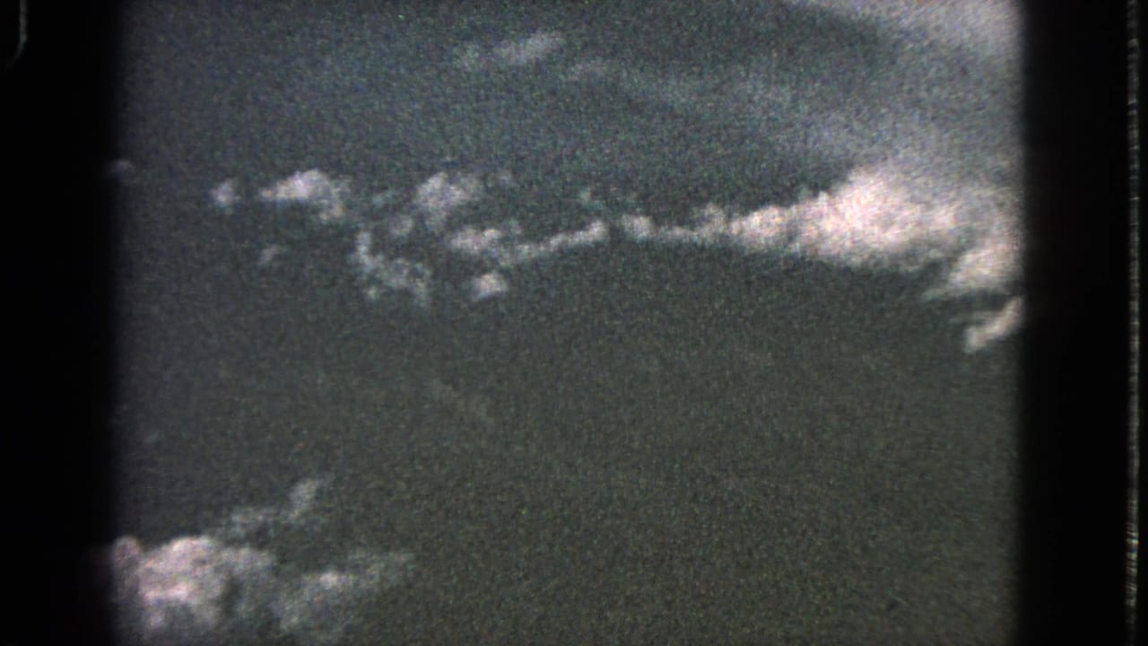 Dark airplane-window view with pale cloud formations across the upper frame.