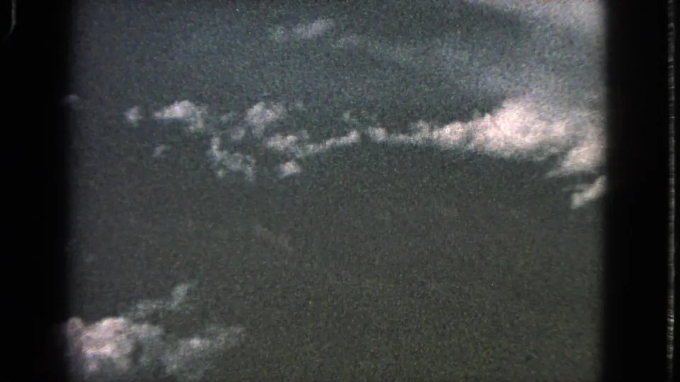 1963 8mm frame showing a grainy passenger-window view of pale cloud bands against a dark sky or ground tone.