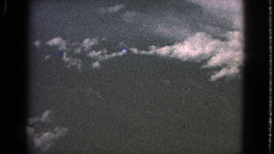 1963 home-movie frame showing cloud clusters and a dark lower field from a fixed airplane-window perspective.