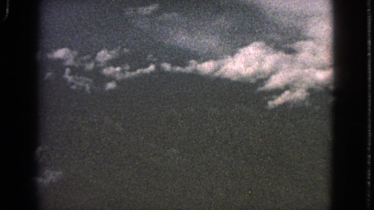 Faded aerial view of clouds and terrain through a dark film frame.