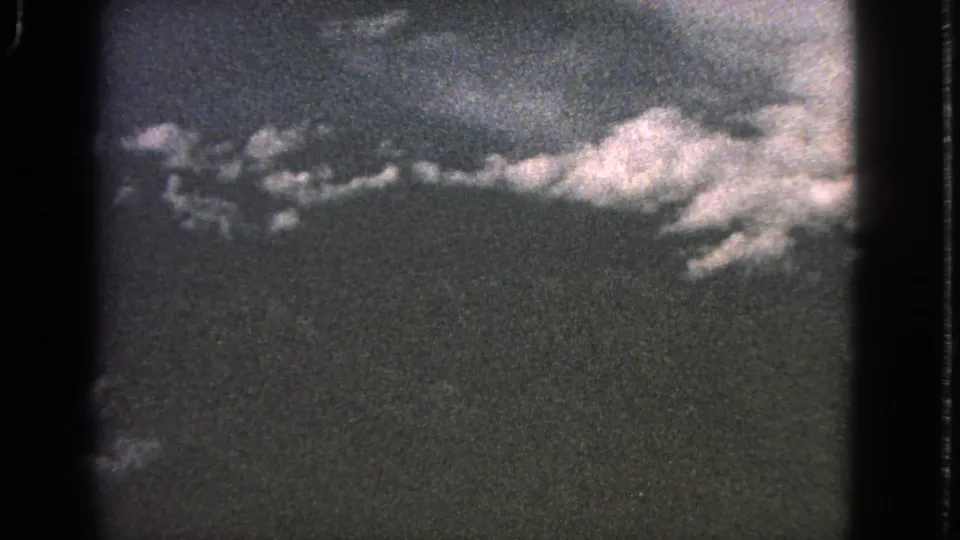 1963 8mm home-movie frame showing a hazy aerial view with clouds, land below, and heavy film grain.