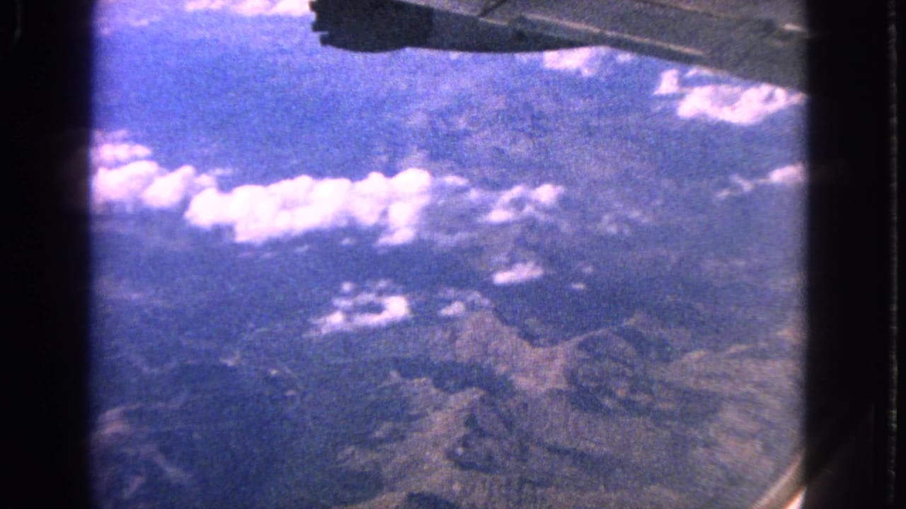 Airplane wing above mountains, clouds, and blue sky.
