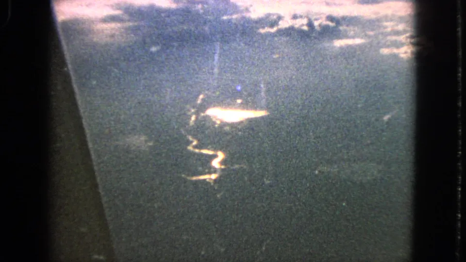 1963 8mm window-seat shot over water, with the sun reflection shifting slightly within the grainy frame.