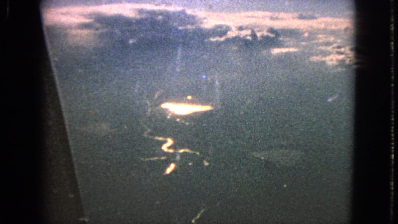 1963 home-movie frame shows a grainy airplane-window view over a reflective river and distant cloudy horizon near Barrington, Illinois by metadata.