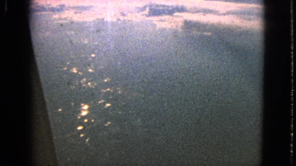 The final 1963 8mm frame holds on a soft airplane-window aerial view with bright water reflections and mottled grain.