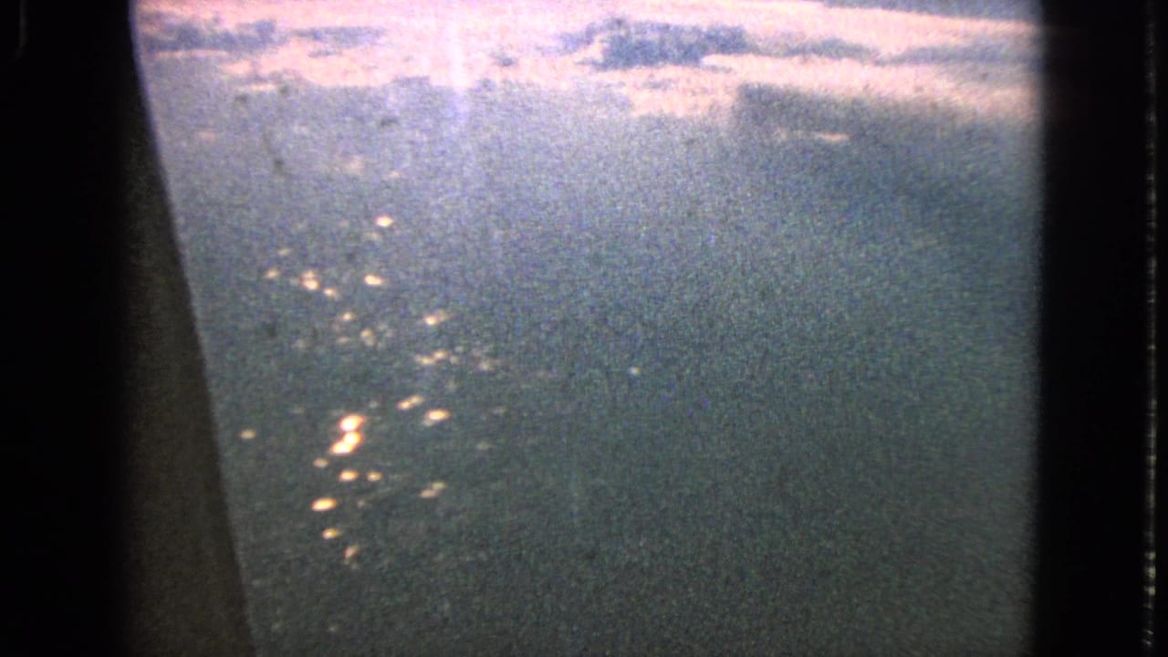 1963 8mm airplane-window view near Barrington, Illinois, showing scattered night lights below through a dark, grainy frame.