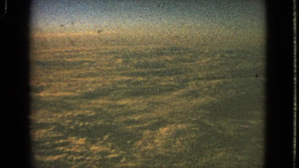1963 8mm frame of a warm, hazy cloudline viewed from an airplane, with grain and visible gate edges.