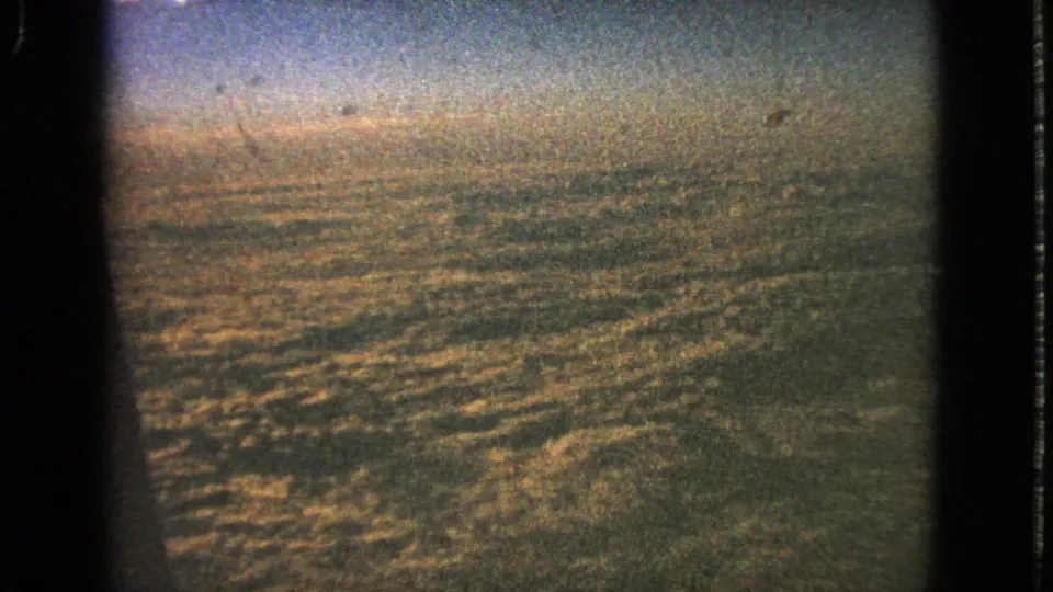 1963 8mm aerial cloudscape with warm sepia color, soft horizon, grain, and dark frame edges.