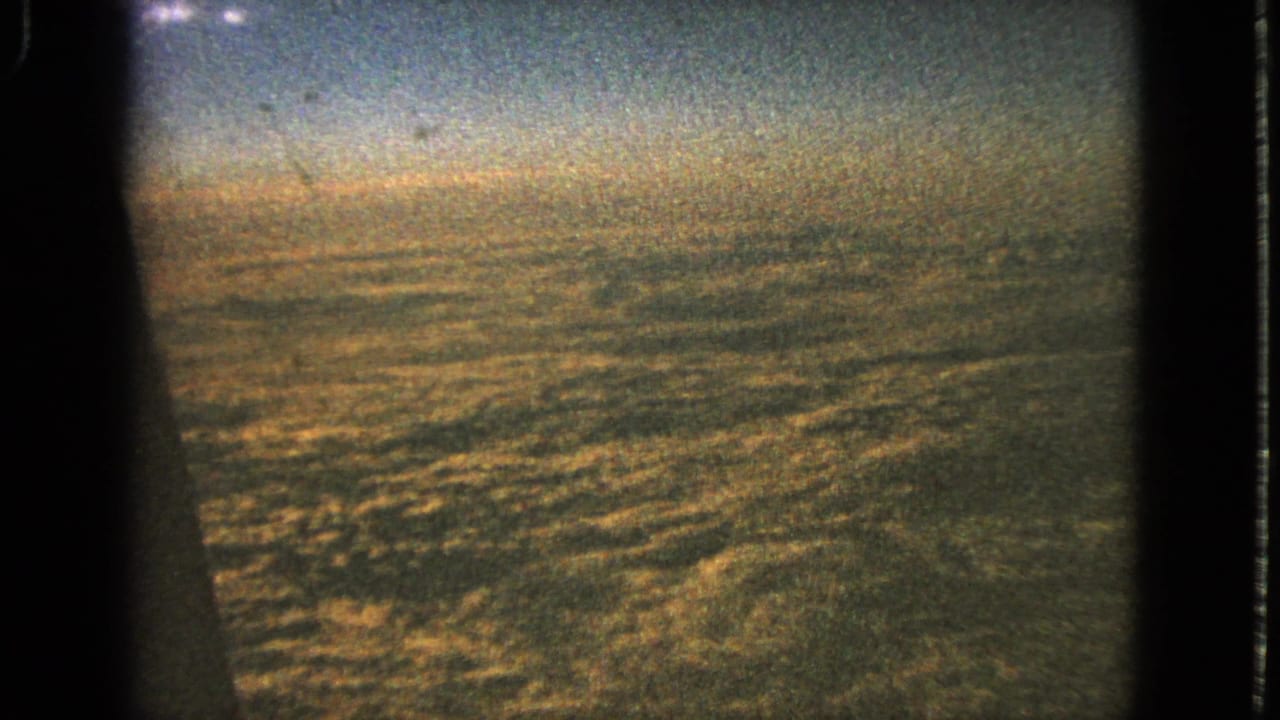 Airplane window view over distant textured ground under a hazy sky.