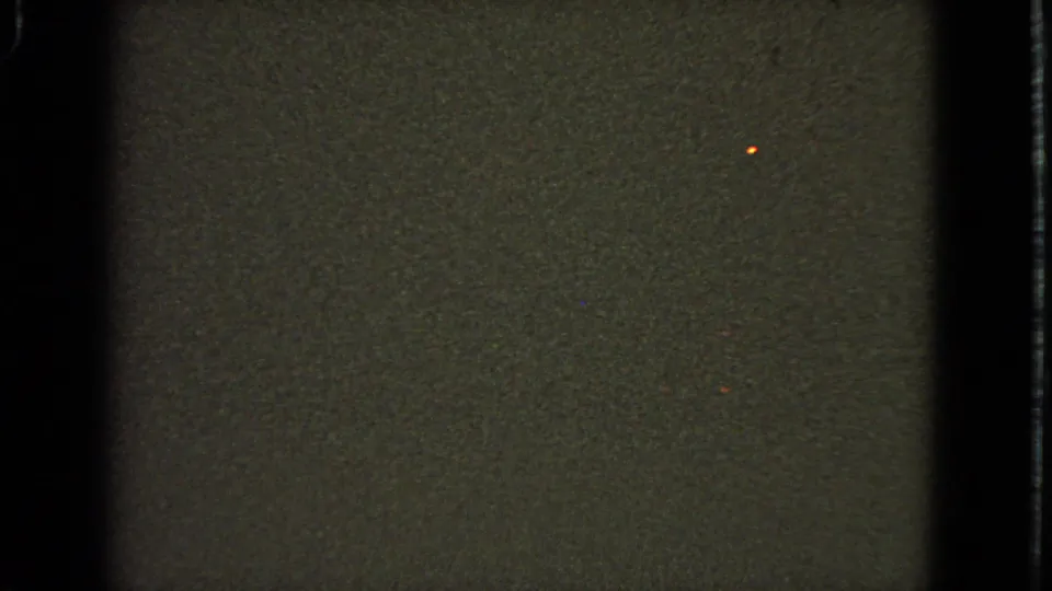 1963 8mm airplane-window view shifts darker, showing faint ground texture, film grain, and a small point of light.