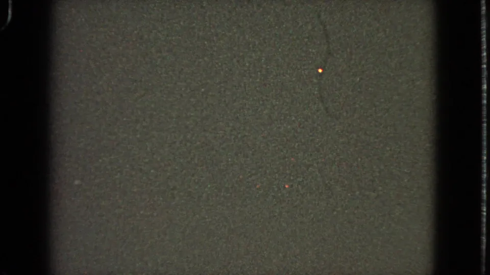 1963 8mm frame showing a dark passenger-window view with grain, muted ground tone, and a small isolated light.